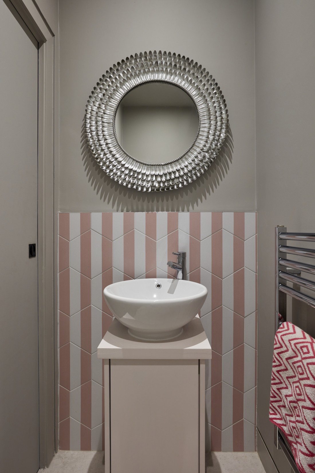 Luxury pool house WC with pink and white stripe tiles and a decorative round mirror.