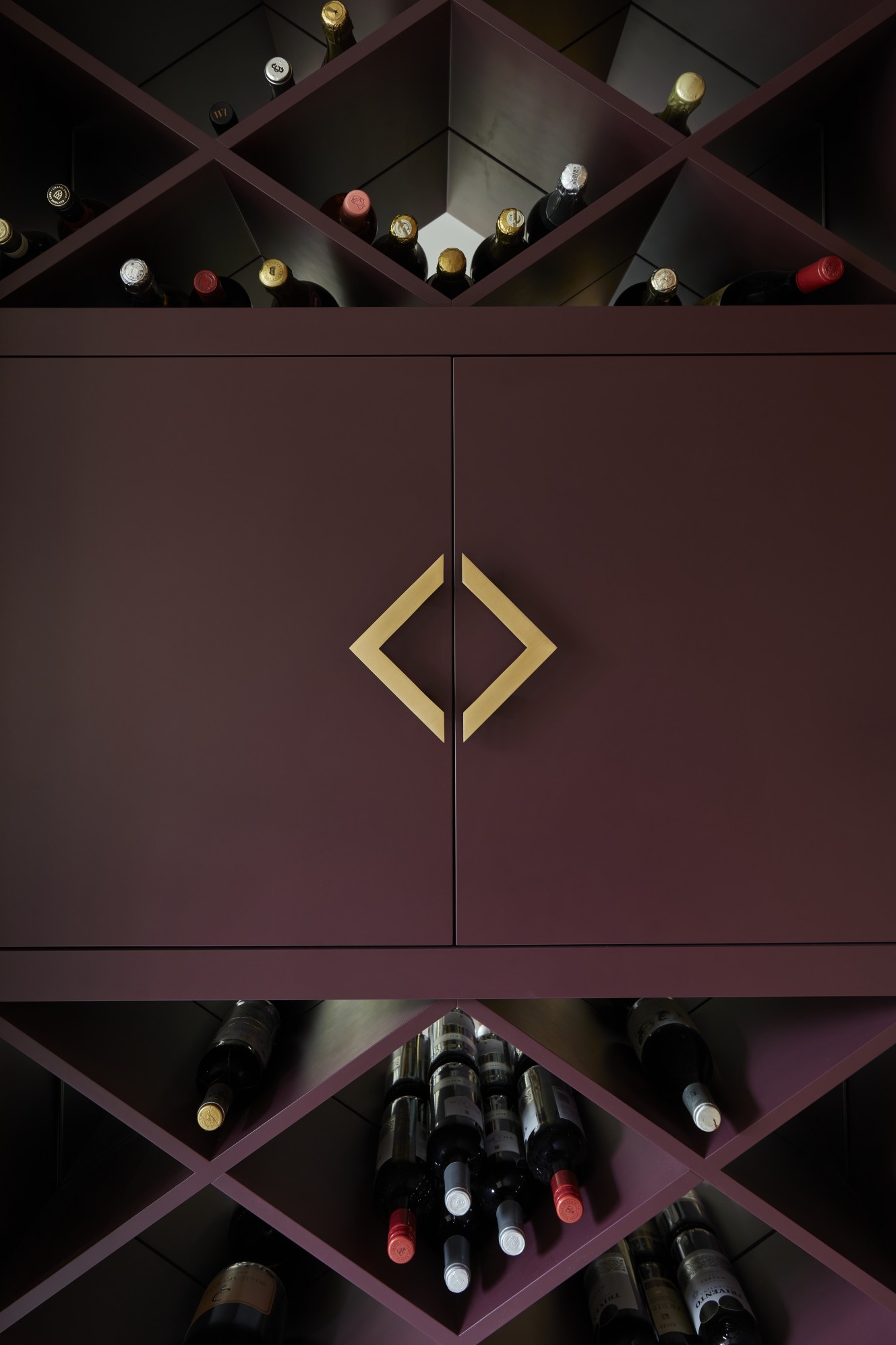 Custom wine storage unit in a burgundy feature wall with angular gold handles in a Surrey manor house.