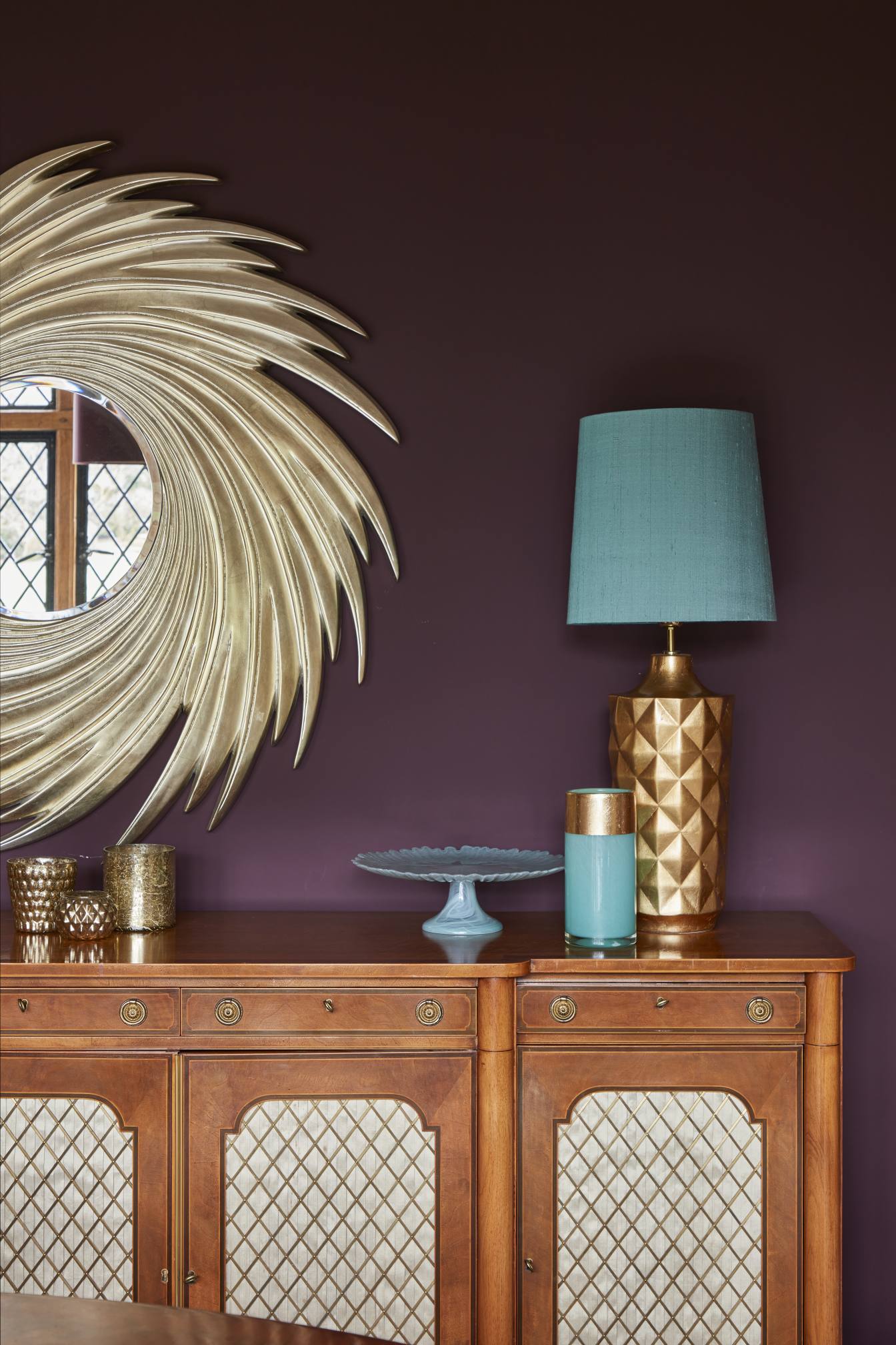 Classic wooden sideboard with gold and teal decor against a burgundy feature wall in a luxury dining room.