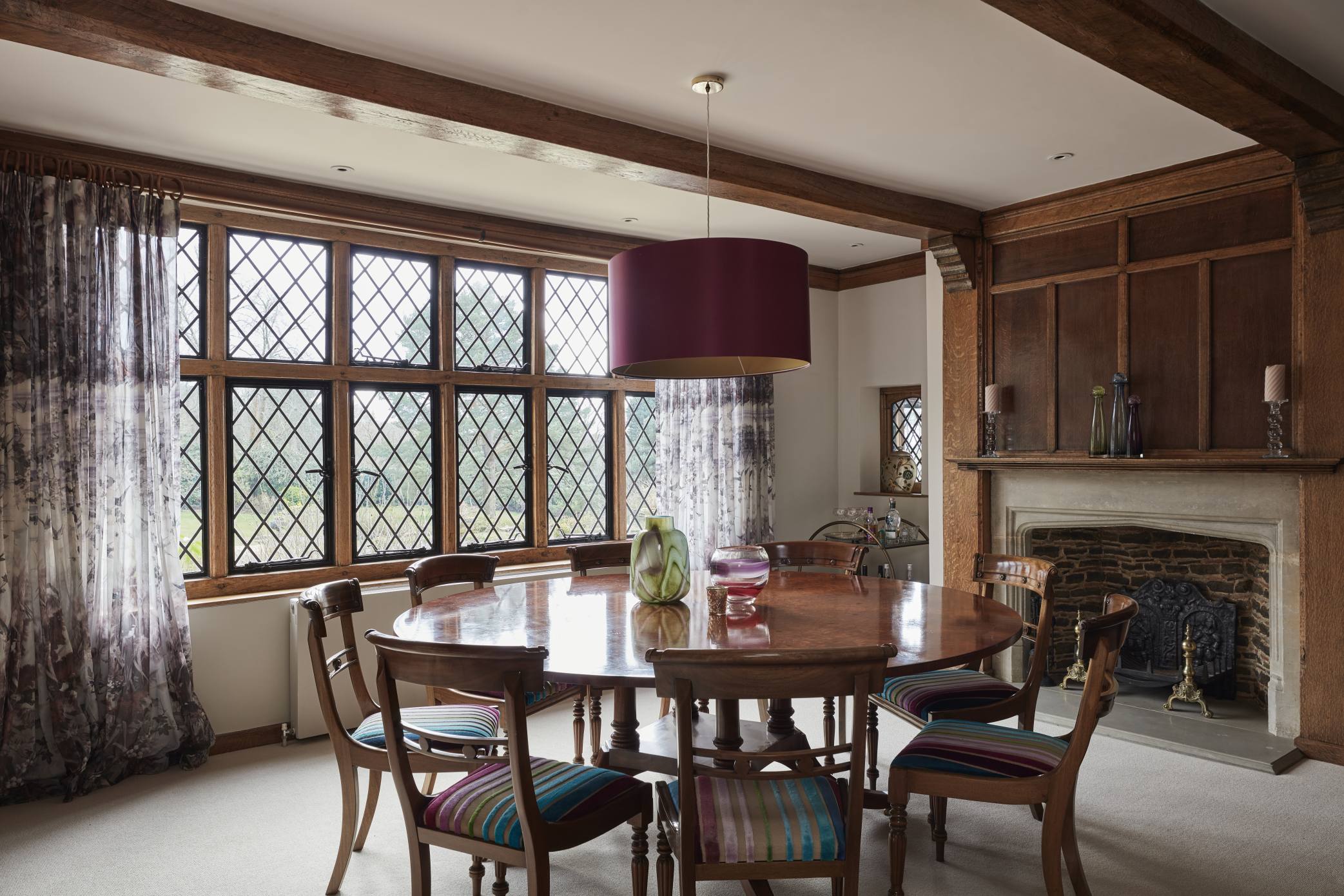 Luxury dining room with antique furniture, a wooden fireplace, and a statement pendant light.