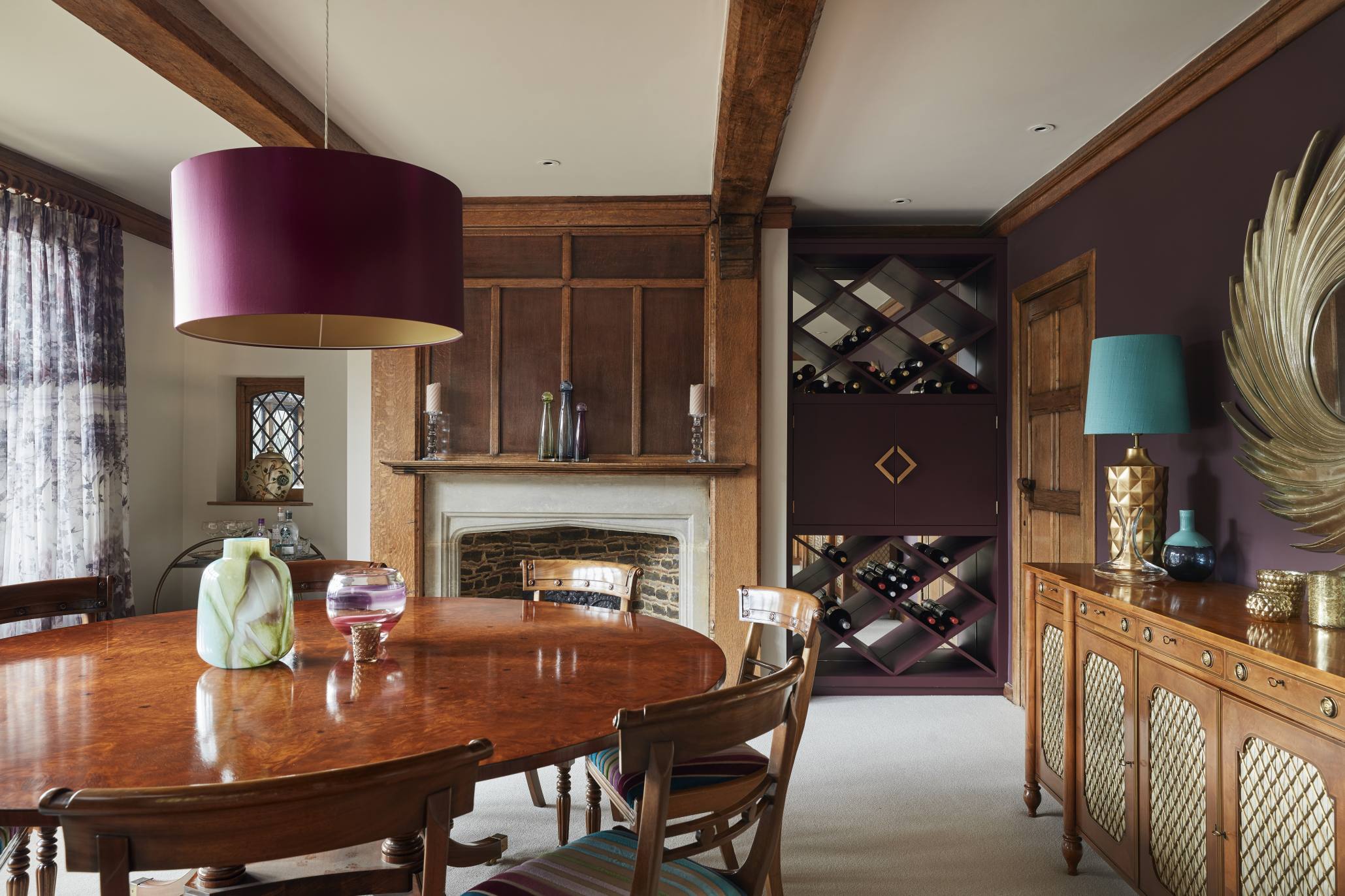 Stylish dining room with bespoke wine storage, antique furnishings, and a grand fireplace in a manor house.