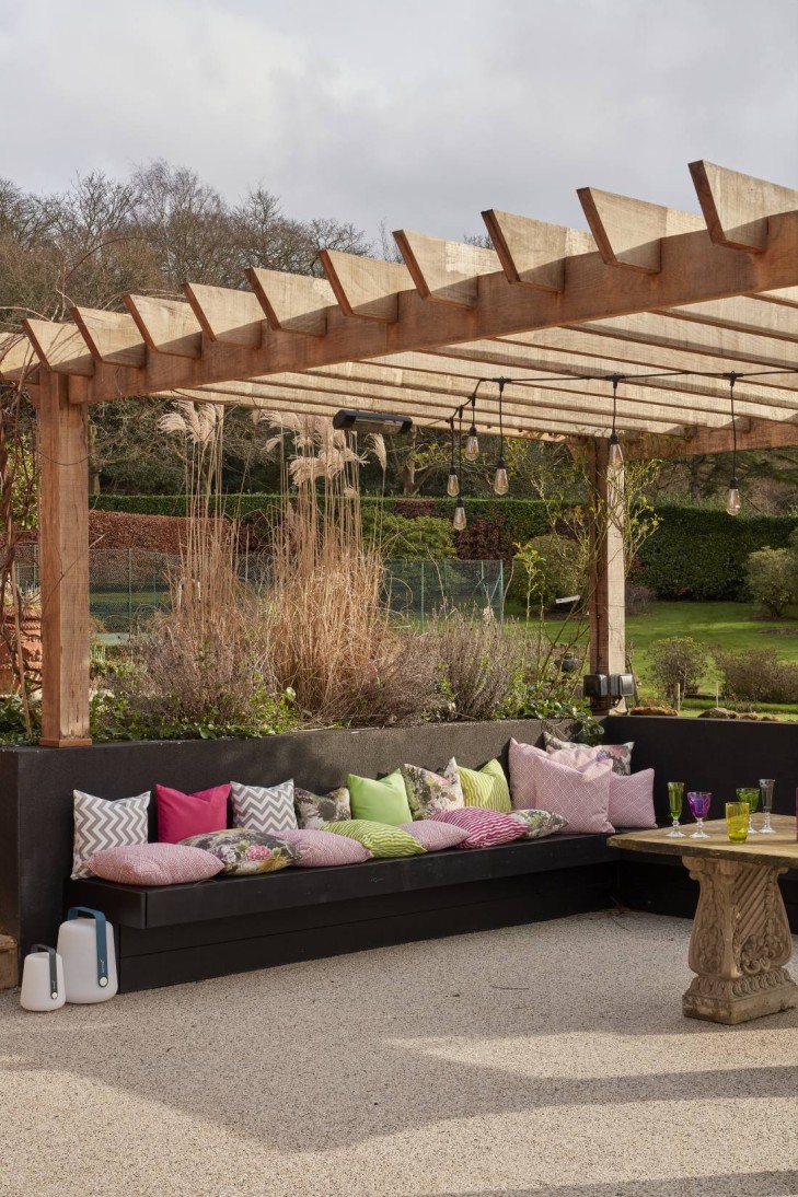 Outdoor seating with a mix of patterned cushions under a wooden pergola in a garden setting.