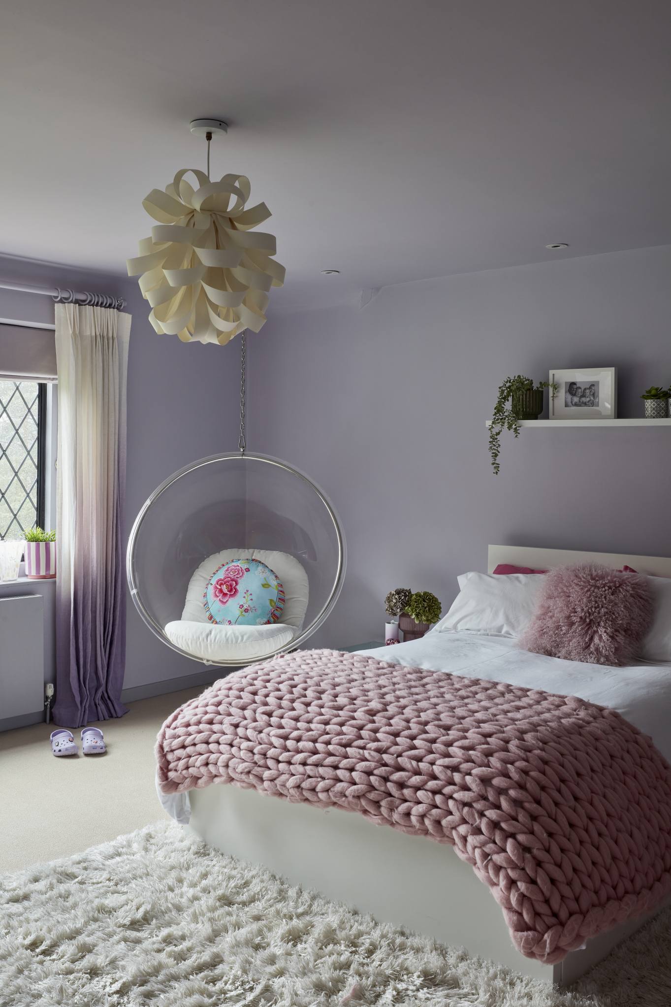 A wider view of a girl's bedroom with a hanging bubble chair, plush pink bedding, and a sculptural ceiling light.