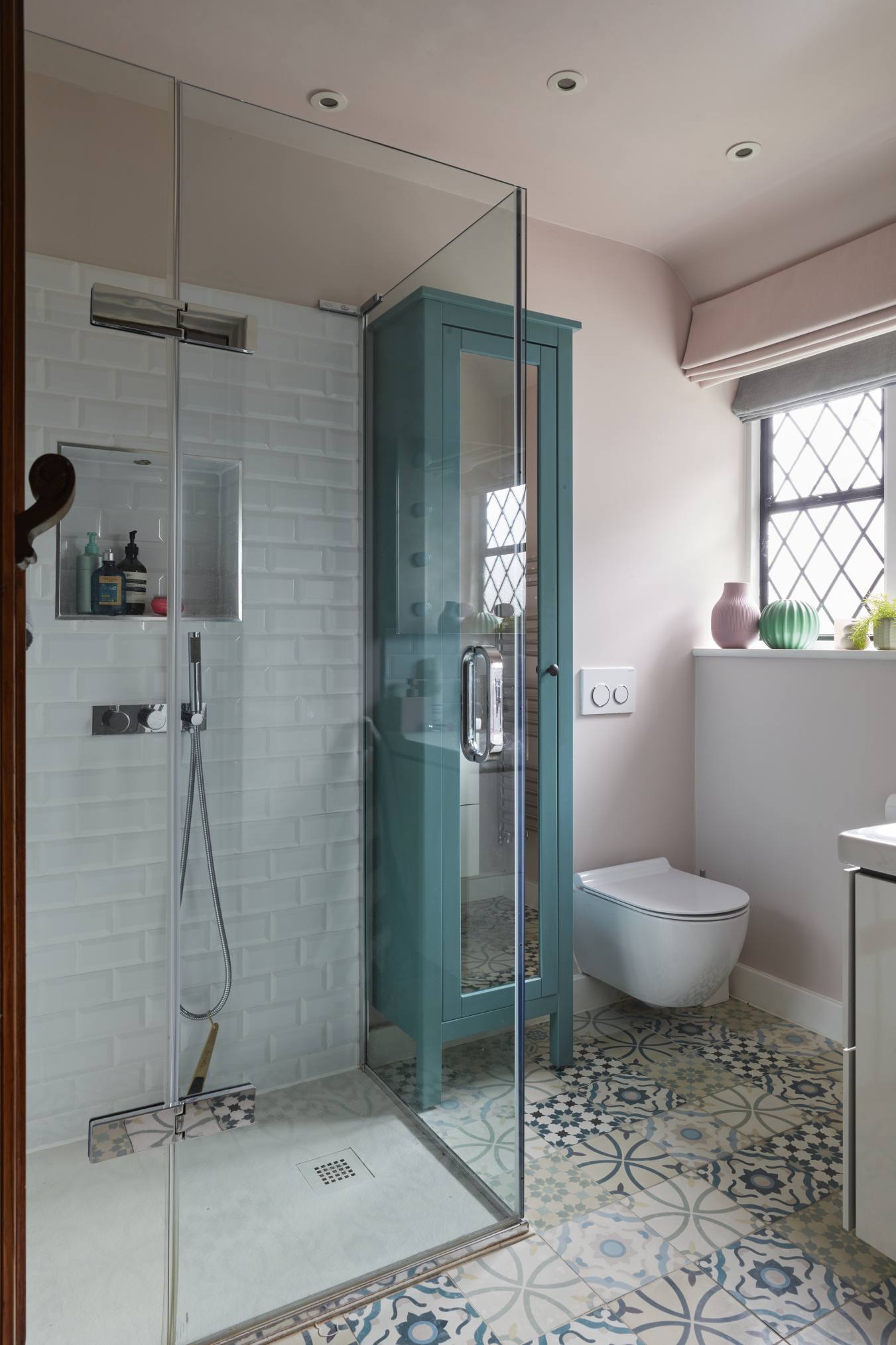 A modern shared shower room with patterned floor tiles, a glass-enclosed shower, and a teal storage unit.