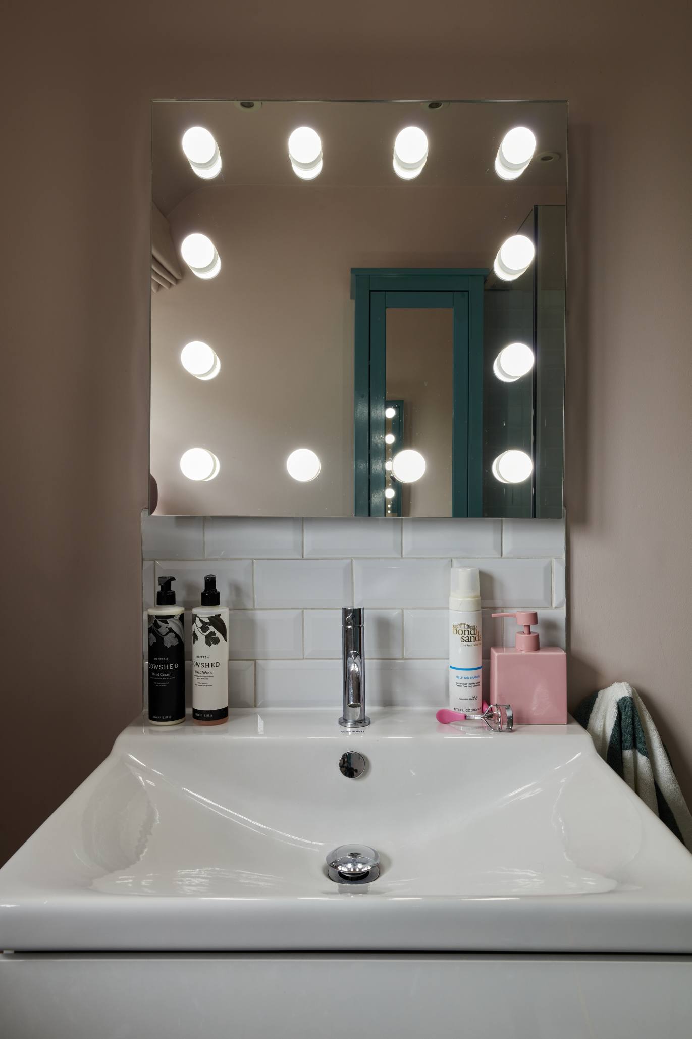 A Hollywood-style bathroom mirror with built-in lighting, a white vanity, and pastel decor accents.