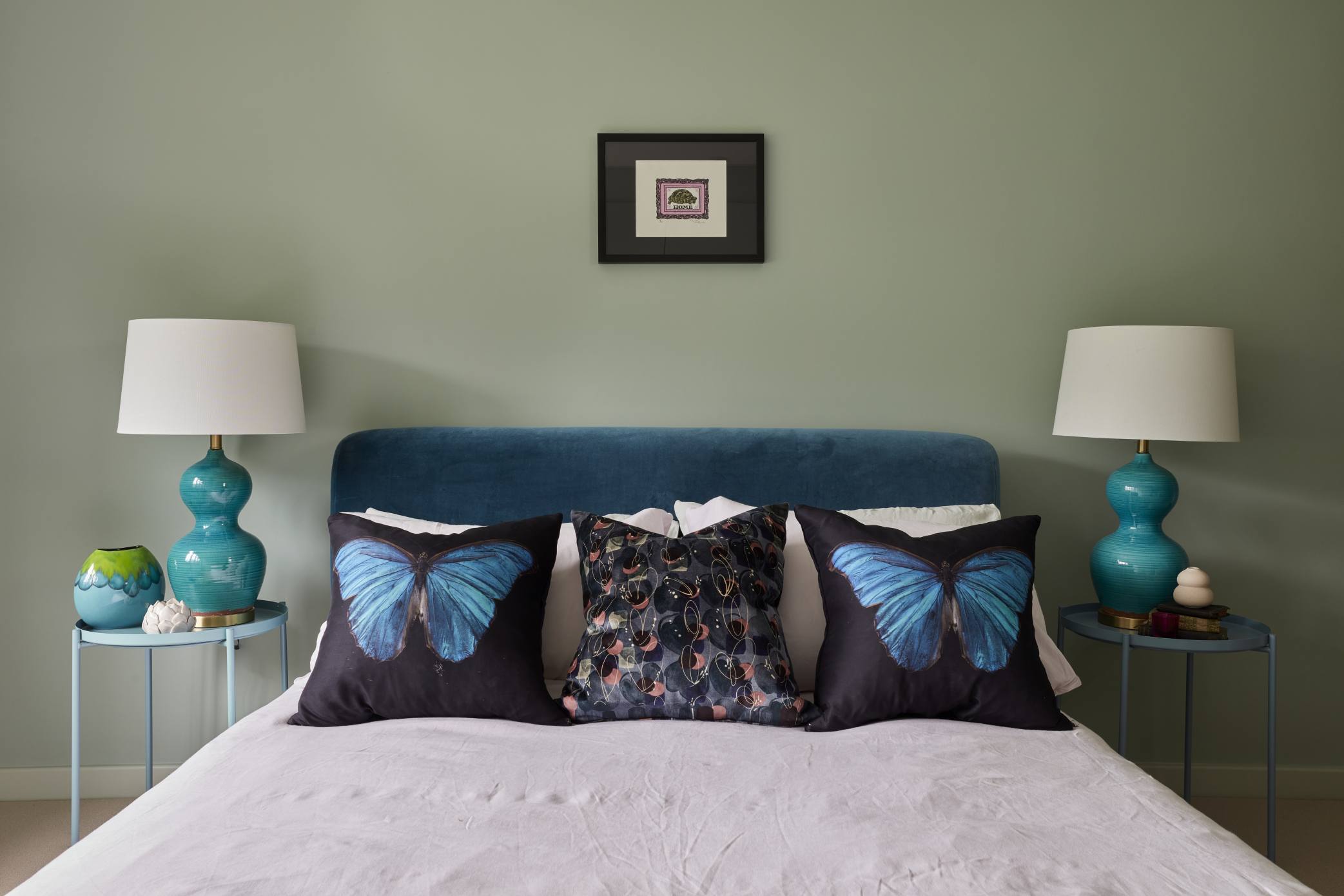 Elegant guest bedroom with a teal velvet headboard, butterfly-themed cushions, and symmetrical bedside lamps.