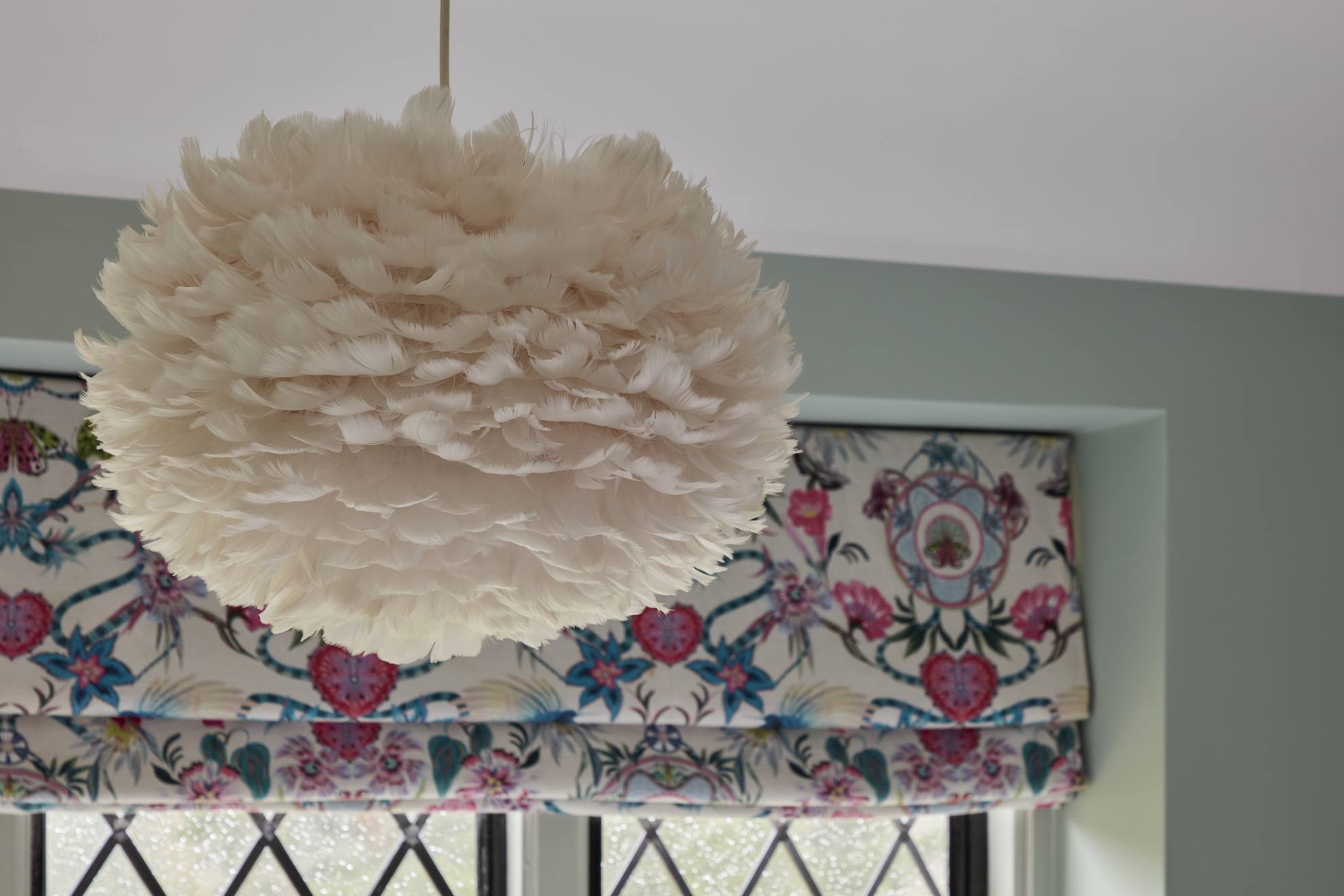 Feathered pendant light with floral Roman blinds in a serene guest bedroom.