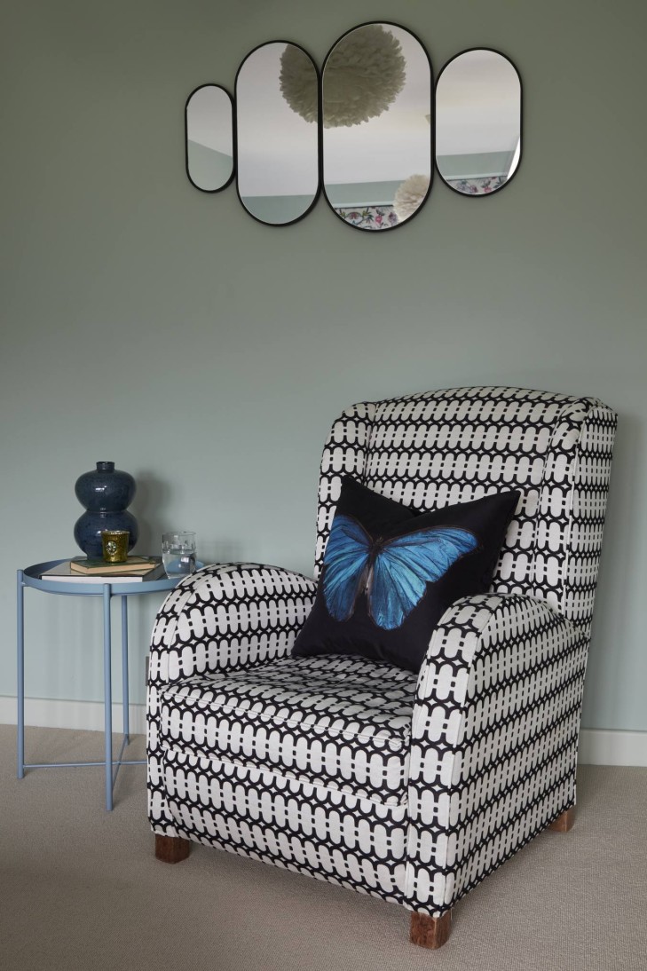 Statement black and white armchair with a butterfly cushion, blue side table, and modern mirror arrangement.