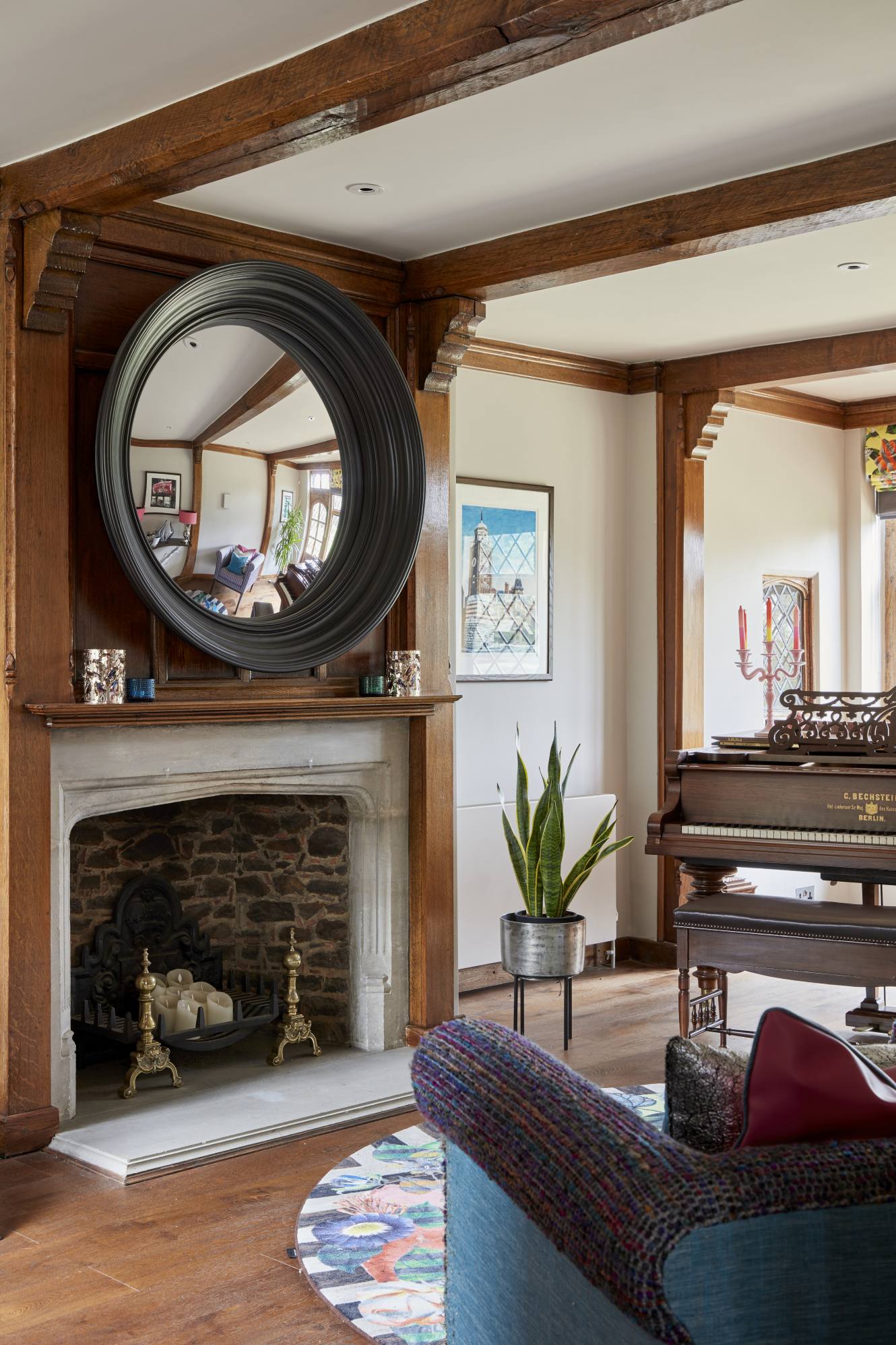 Luxury entrance hall with a stone fireplace, convex mirror, and grand piano reflection in a Surrey manor.