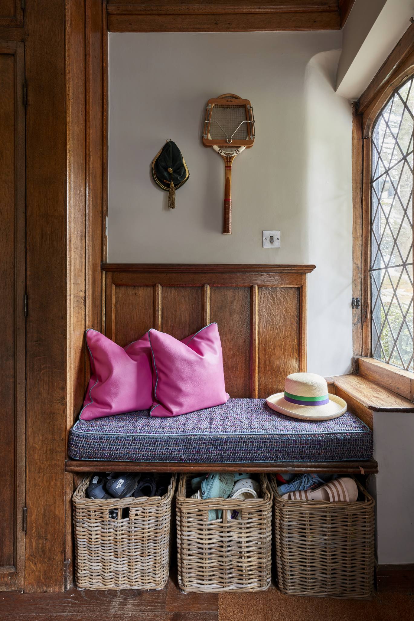 Cozy built-in bench with woven storage baskets and vibrant pink cushions in a countryside home.