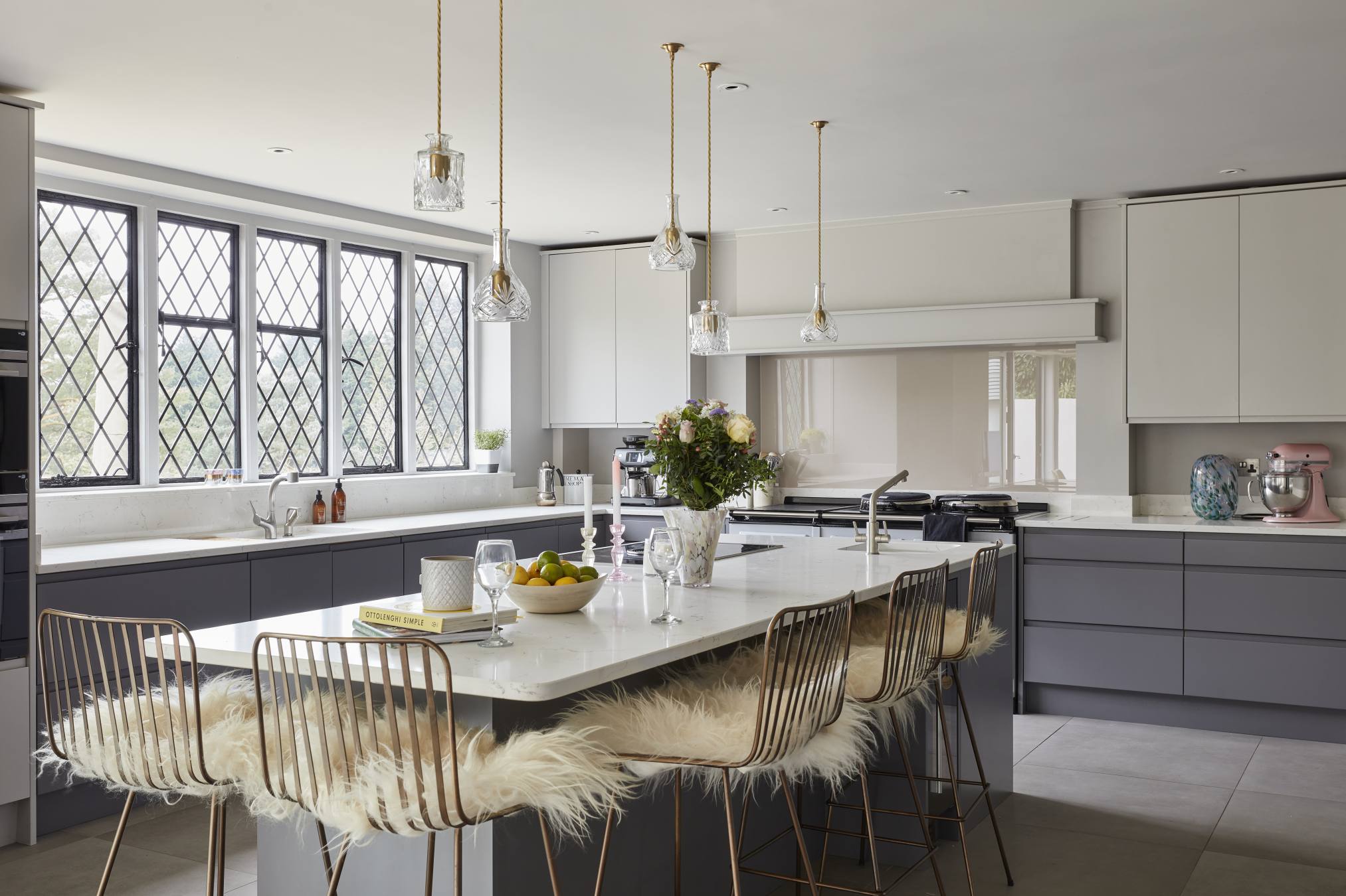 Luxury kitchen in a Surrey manor house with a large island, gold pendant lights, and fur-lined stools.