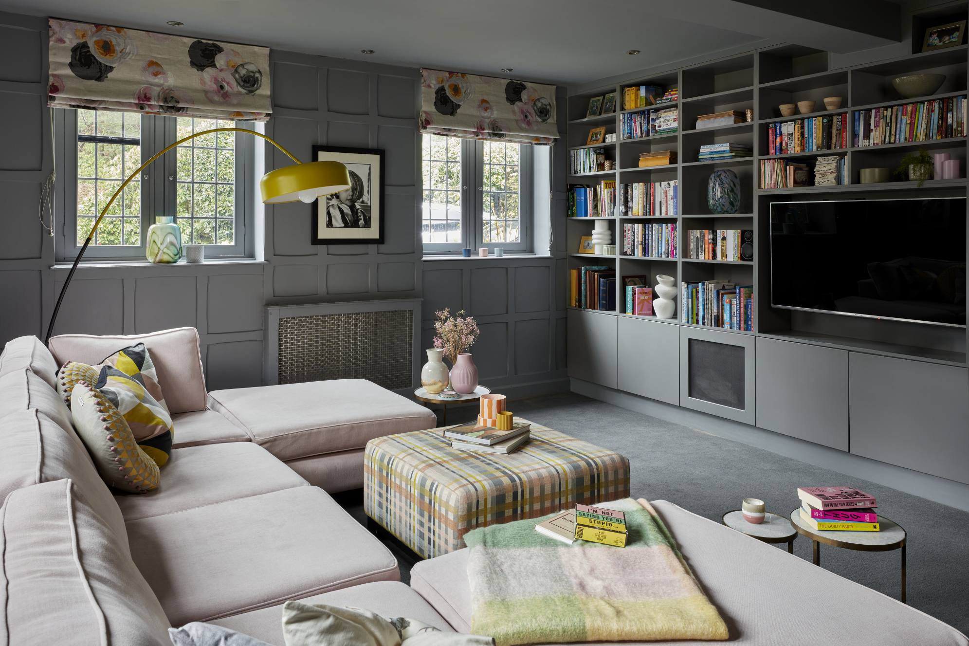 Luxury home library with bespoke grey cabinetry, soft pink sofa, and patterned ottoman in a Surrey manor house.