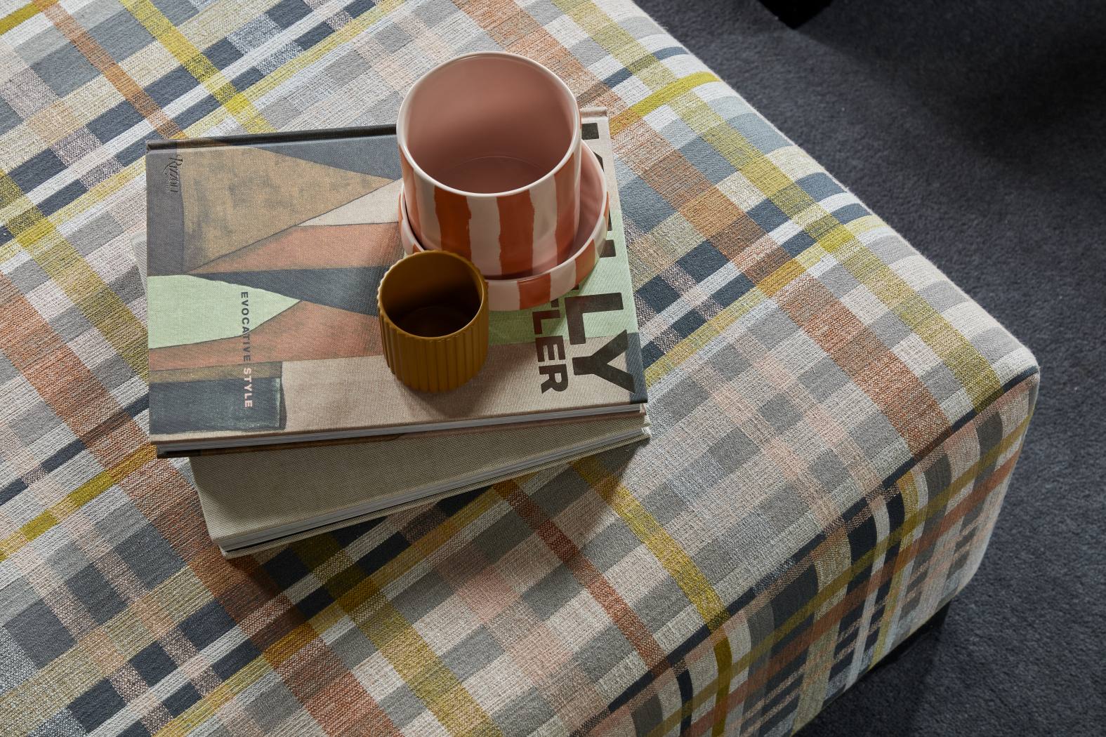 Close-up of a plaid ottoman with stacked books and ceramic décor in a countryside home library.