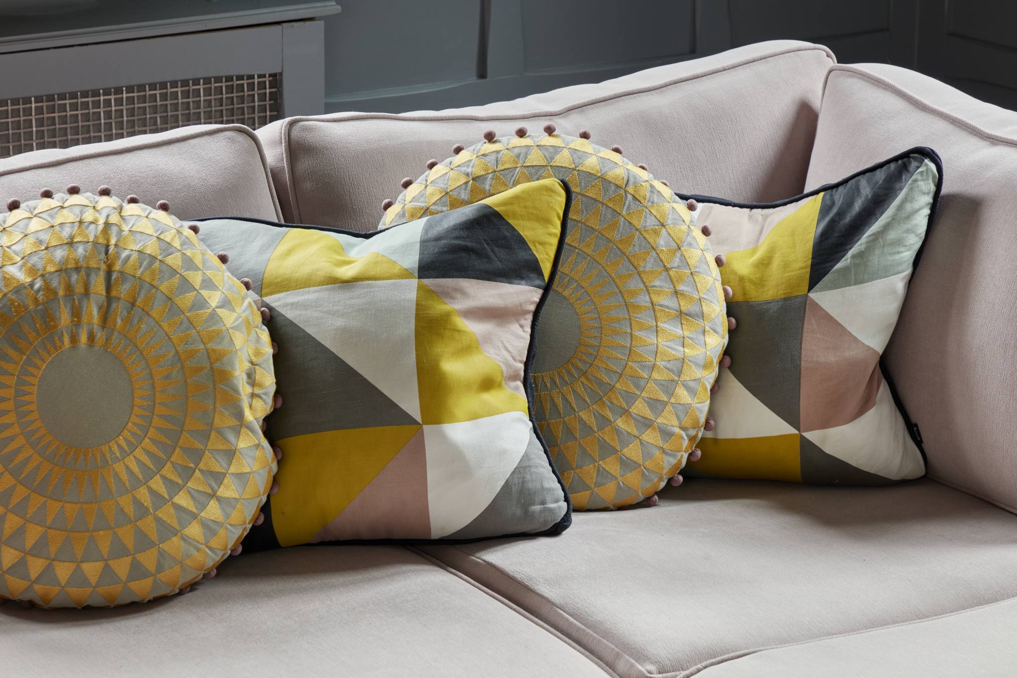 Geometric and embroidered cushions in yellow and pink on a soft pink sofa in a luxury home library.