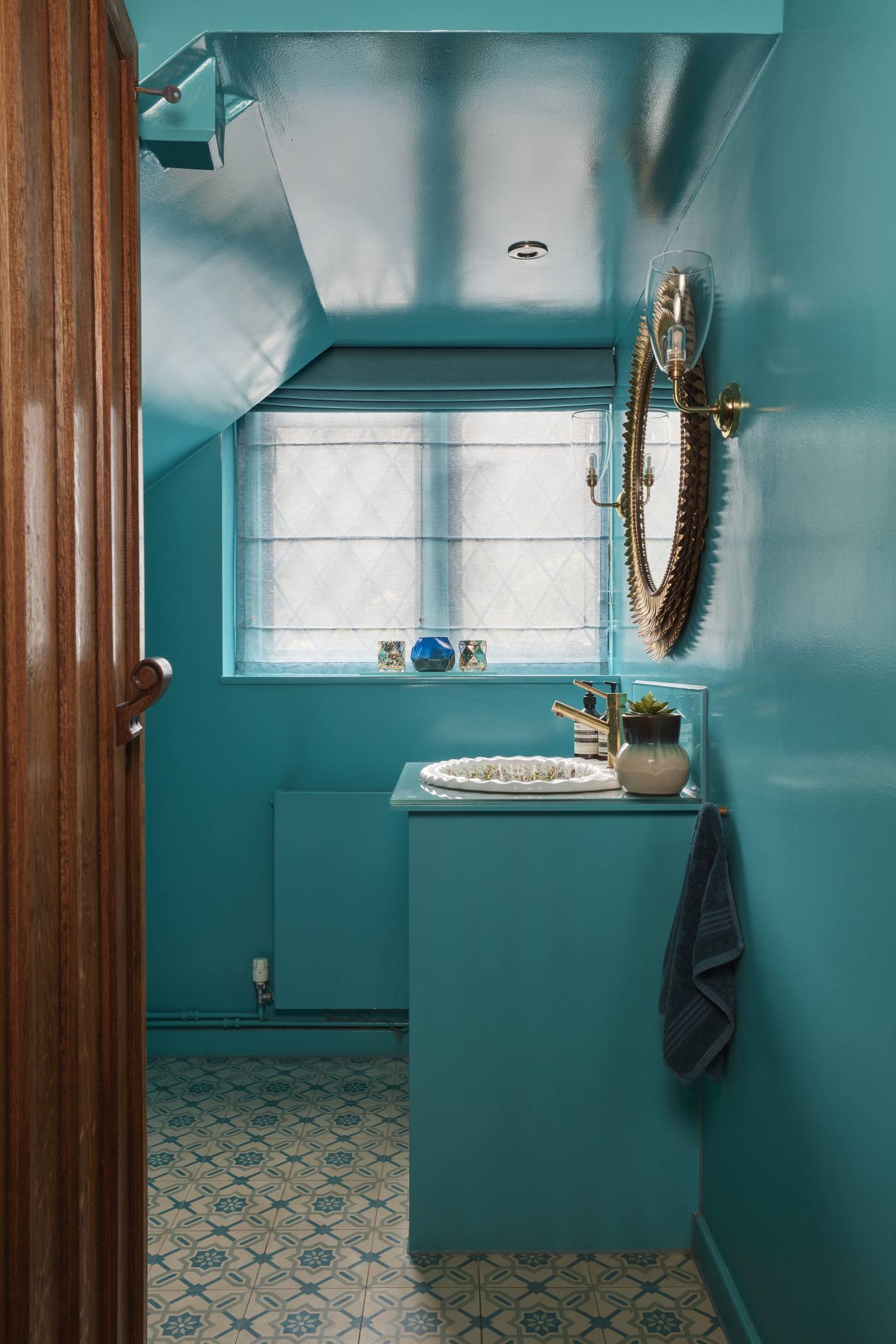 Vibrant turquoise guest loo in a luxury Surrey manor house, featuring glossy walls, a gold mirror, and eclectic tiles.