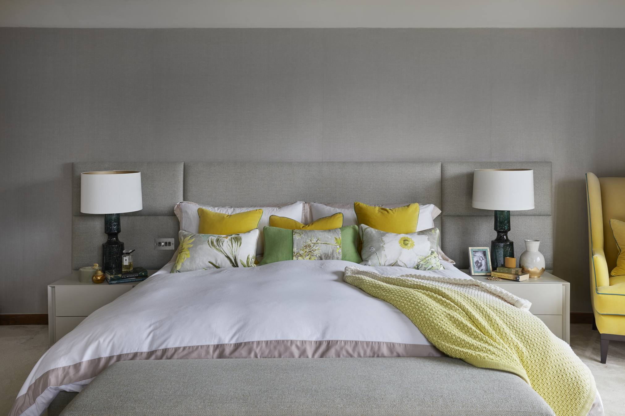 Luxurious master bedroom with a custom-designed headboard and plush bedding in neutral tones with pops of yellow and green.