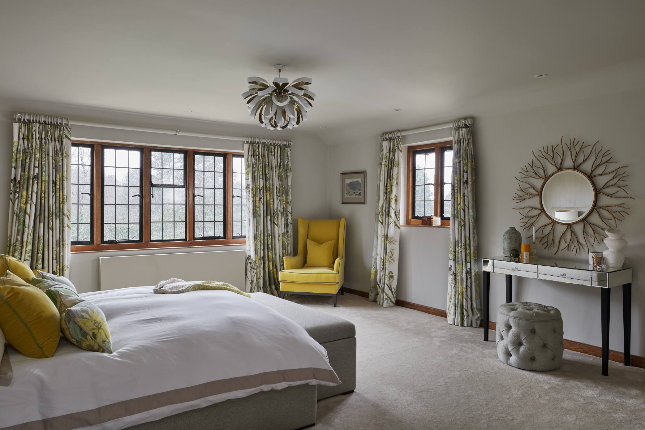 Spacious master bedroom with large windows, a yellow accent chair, and mirrored dressing table.