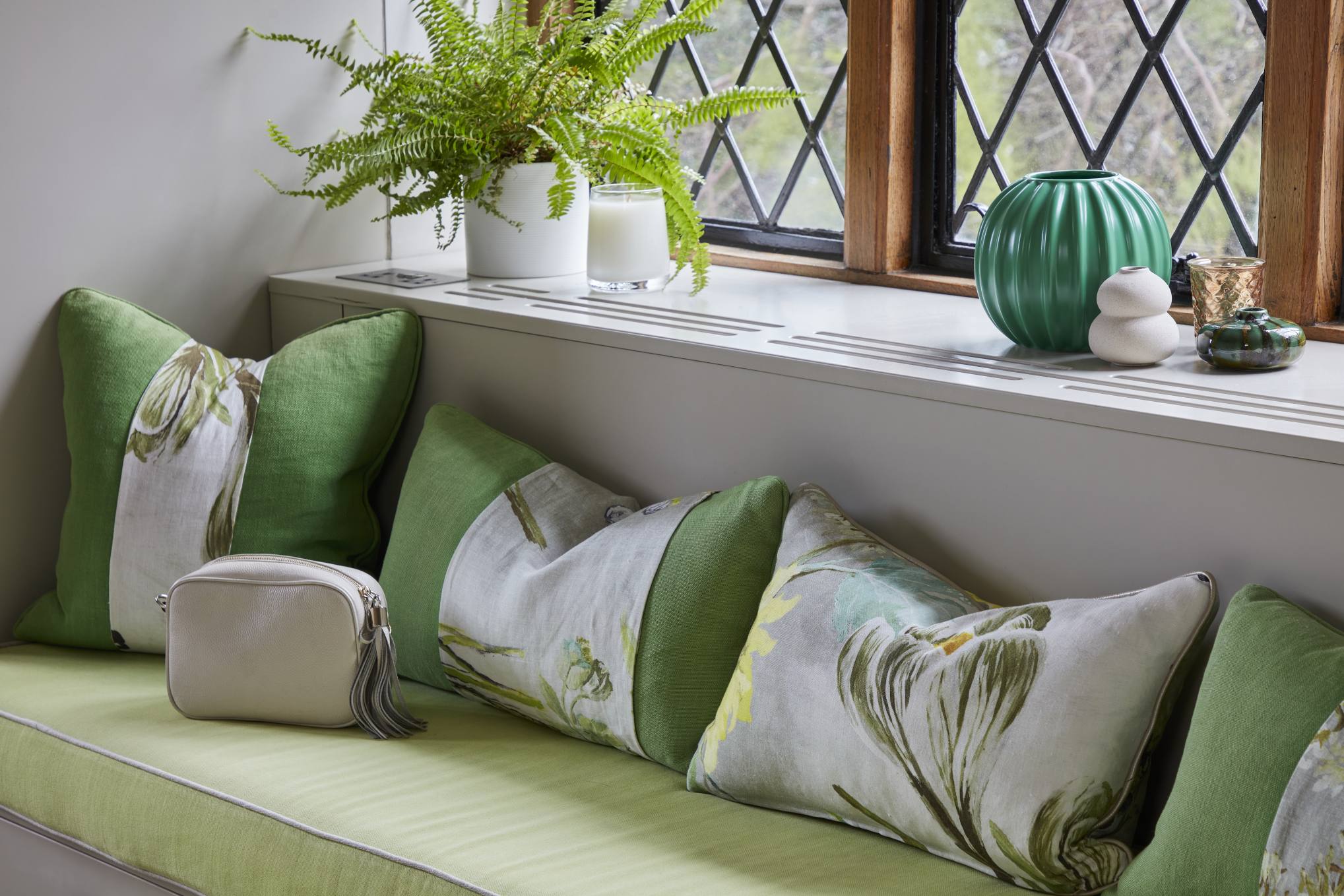 Cozy window seating area with floral and green cushions, surrounded by natural light.