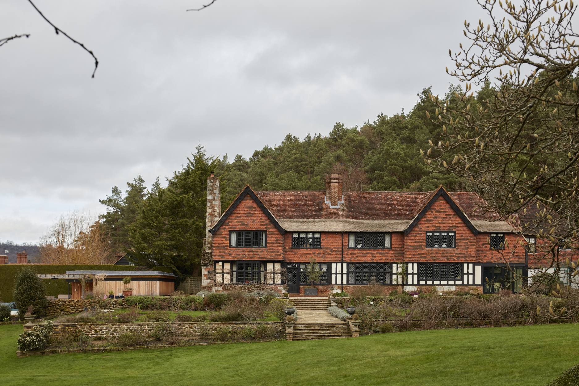 Rear view of a historic manor house in the Surrey countryside with landscaped gardens and a modern pool house.