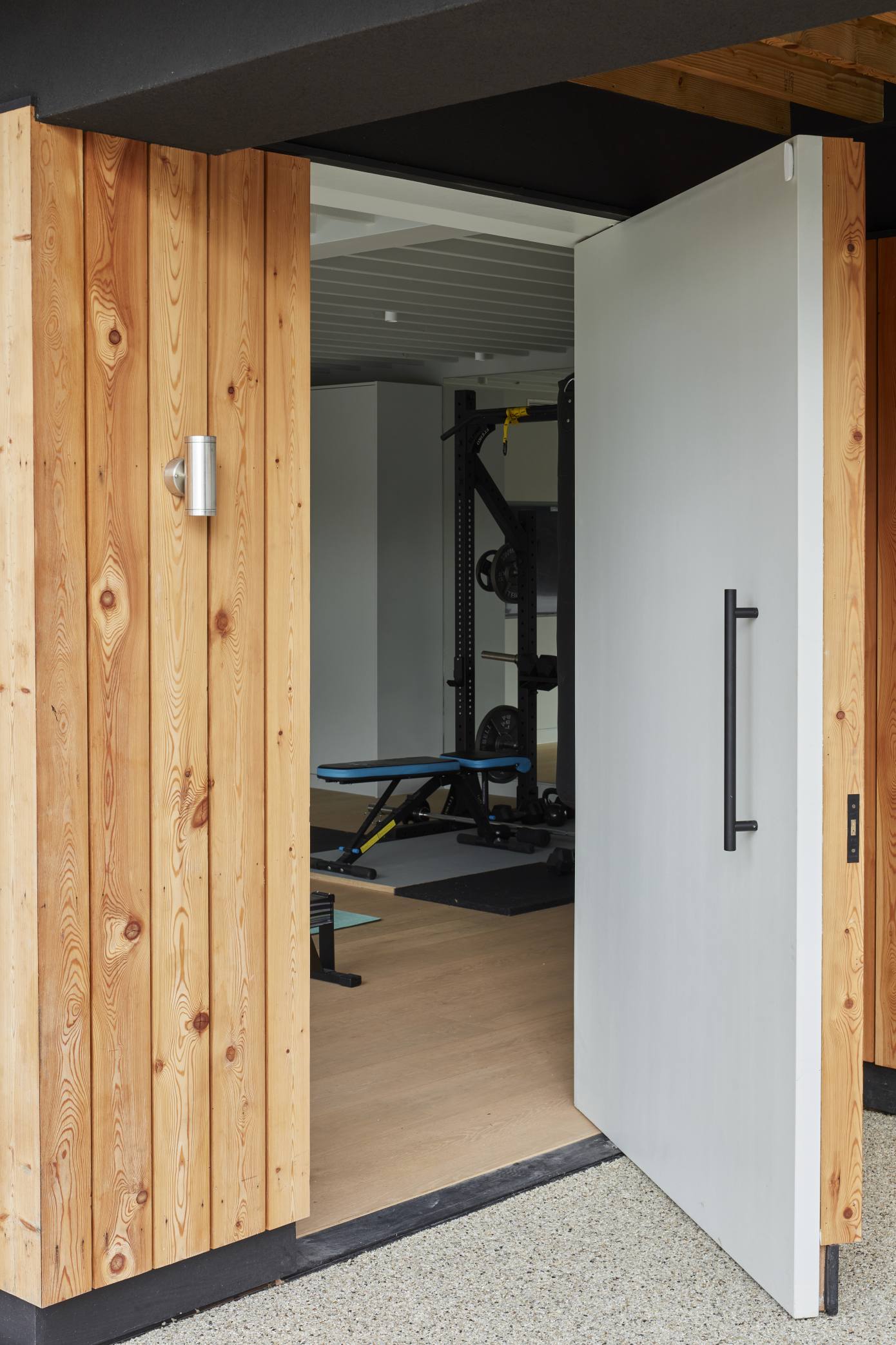 Open doorway revealing a luxury home gym in a modern pool house