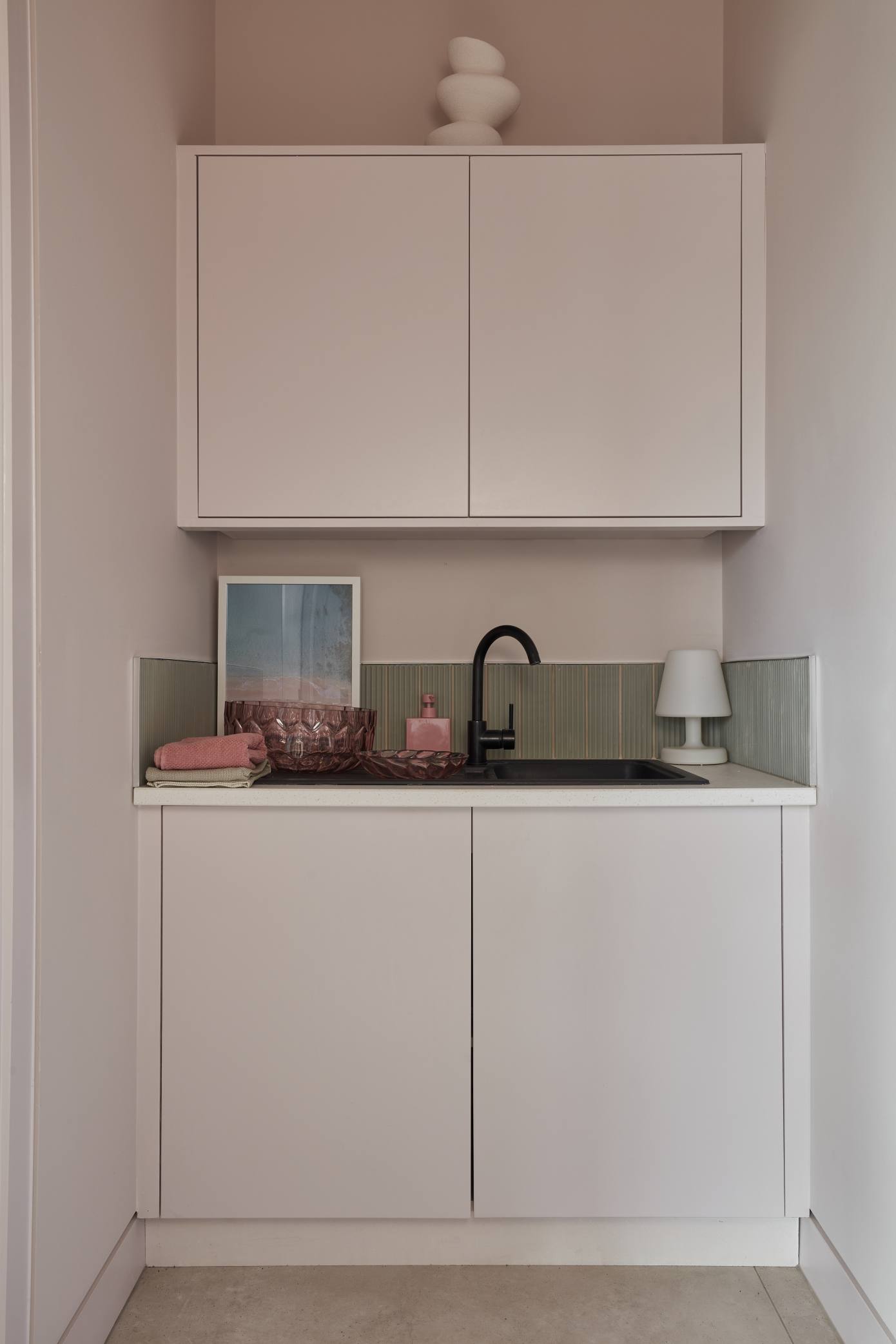 Compact kitchenette in the pool house with soft pink cabinetry and a black sink