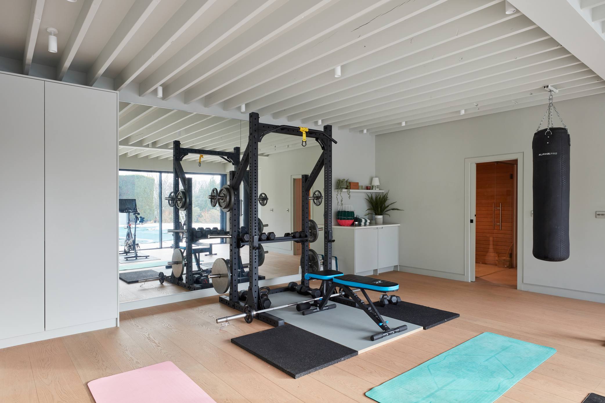 Home gym with weightlifting station, yoga mats, and a sauna entrance.