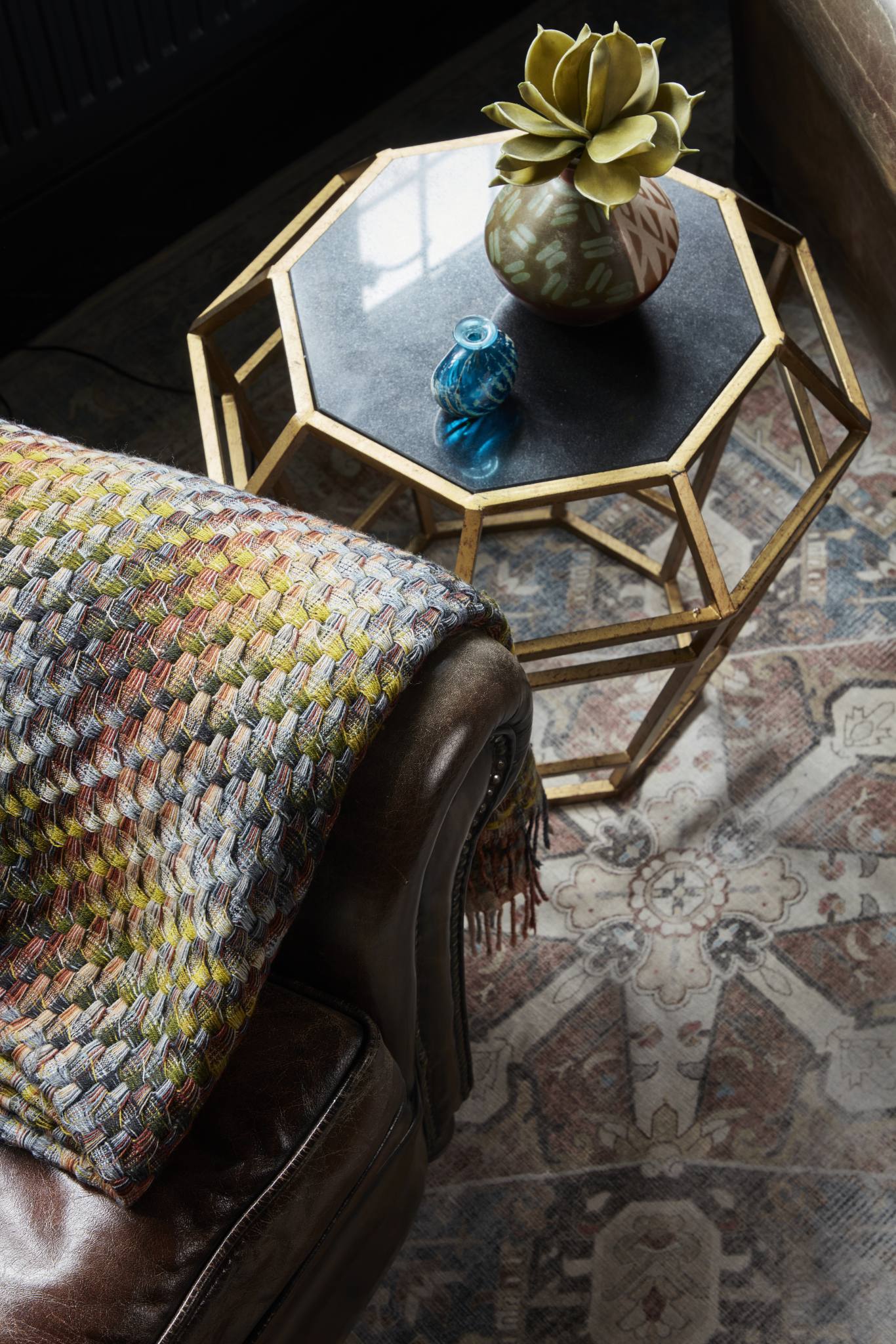 Close-up of a vintage leather armchair with a woven throw and brass side table in a countryside house study.