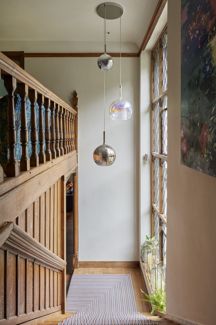 Grand wooden staircase in a Surrey manor house with a bespoke runner and glass pendant lighting.